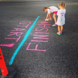 Siblings creating a start and finish line with spray paint.  Creating an imaginary place to have a race.  This image depicts a manner in which siblings can engage in pretend play.